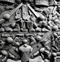 A complex arrangement of various sports equipment and attire, including tennis rackets, soccer balls, basketballs, helmets, shoes, gloves, and a mannequin torso wearing a T-shirt. The items are layered and artistically displayed in a monochrome color scheme, creating an intricate texture and visual pattern.